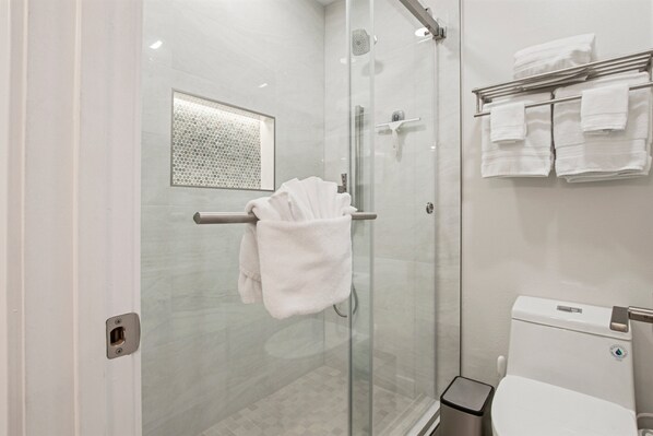Ein modernes Badezimmer mit Duschkabine aus Glas, Toilette und Handtuchhalter mit Handtüchern.