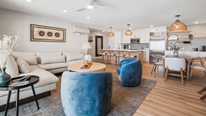 A modern living room with a sofa, blue armchairs, a coffee table, and a dining area with a table and chairs. - Heart of La Jolla Gem - Newly Renovated! (La Jolla)
