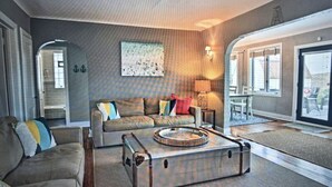 A living room with a sofa, a coffee table, and a suitcase. There is a painting on the wall and a lamp on a side table. - Charming Beachfront Home, large backyard and deck, walk over dune to stop2 beach (Michigan City)