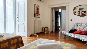 A hotel room with two beds, a radiator, an air conditioning unit, a framed picture on the wall, and a sofa with a patterned cover. - Elegant And Spacious Apartment In The Very Historical Centre Of Naples (Napoli)