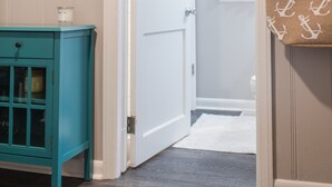 A hallway with a teal cabinet, a white door, and a hanging bag with anchor prints. - North End Beach Cottage Apartment - One block from beach (Virginia Beach)
