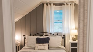 A bedroom with a bed, bedside tables, and a window with curtains. - North End Beach Cottage Apartment - One block from beach (Virginia Beach)