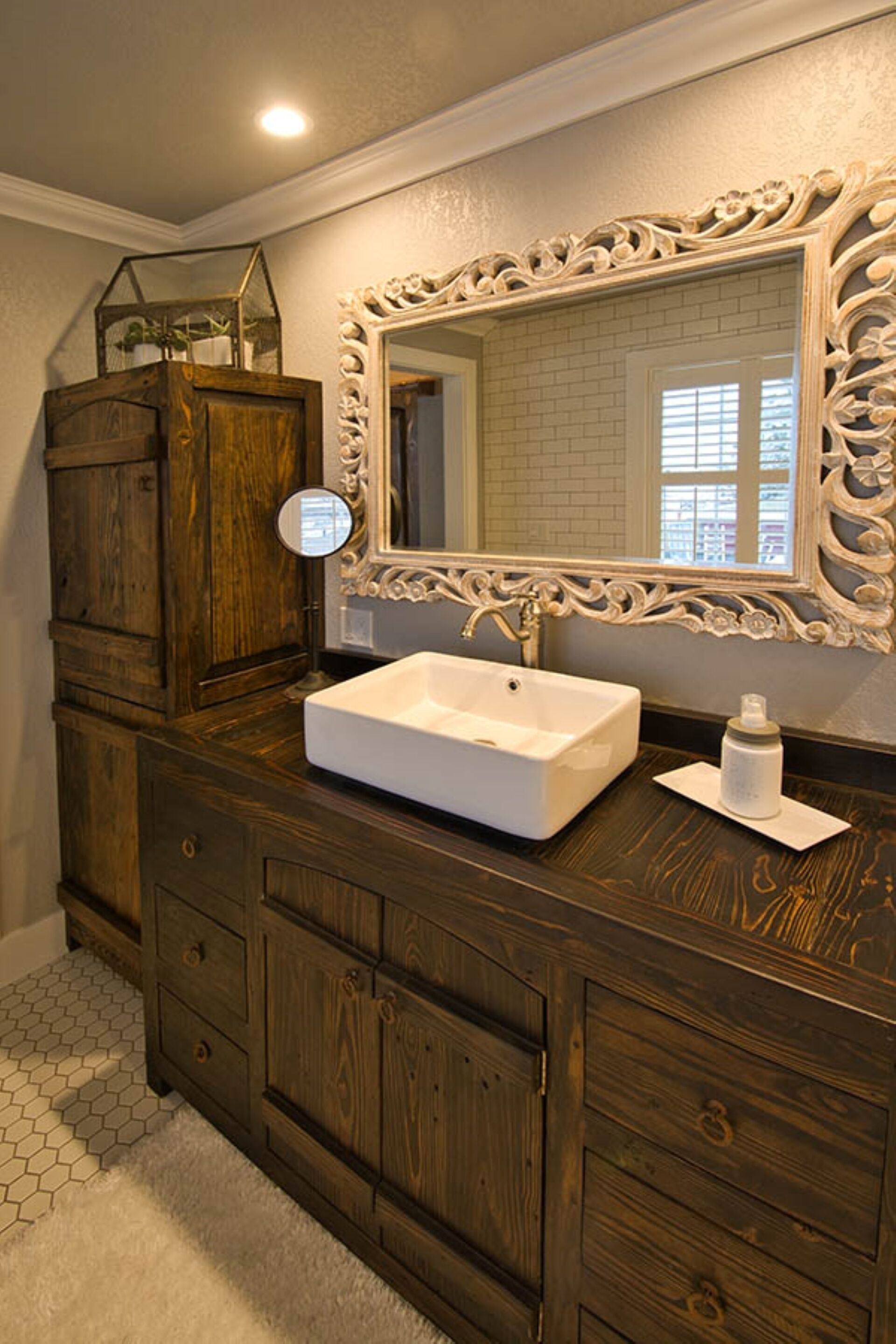 A bathroom with a wooden vanity, a white sink, and a large mirror with an ornate frame.