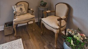 Une pièce dotée d’un plancher en bois, de deux chaises de style vintage, d’un lustre, d’une horloge murale et d’une plante en pot.