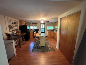 Une cuisine de taille réduite, dotée de meubles en bois, d’un réfrigérateur, d’une table à manger avec des chaises et d’un ventilateur de plafond.