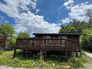A wooden cabin with a deck, surrounded by greenery and trees.