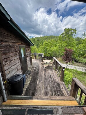 Eine Holzterrasse mit Tisch, Stühlen, einem Mülleimer und einer Tür zu einer Hütte.