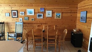 A wooden cabin interior with a dining table and chairs, a refrigerator, and a wall adorned with framed pictures. - Cute Lakefront Cottage on Lake Michigan.   (Mears)