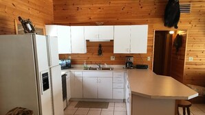A compact kitchen with white cabinets, a refrigerator, a coffee maker, and a sink. - Cute Lakefront Cottage on Lake Michigan.   (Mears)