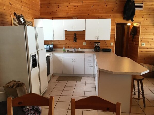 A compact kitchen with white cabinets, a refrigerator, a coffee maker, and a sink.