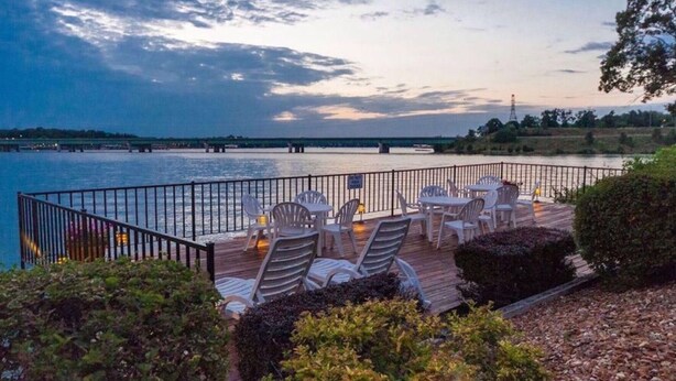 A deck with outdoor seating overlooking a body of water, a metal railing, and a distant bridge. - Freshly Remodeled Condo with amazing Grand Glaze View! (Osage Beach)