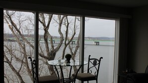 A room with a large window overlooking a river and a bridge. There is a table with chairs and a small plant on it. - Freshly Remodeled Condo with amazing Grand Glaze View! (Osage Beach)