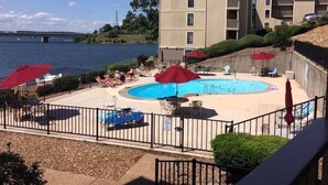 A pool area with red umbrellas, lounge chairs, and a view of a body of water. - Freshly Remodeled Condo with amazing Grand Glaze View! (Osage Beach)