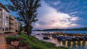 A waterfront property with a dock and boats, a large tree, and a building with balconies. - Freshly Remodeled Condo with amazing Grand Glaze View! (Osage Beach)