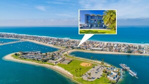 Vue aérienne d’une zone côtière comprenant un port de plaisance, un quartier résidentiel et un bâtiment moderne mis en valeur, avec un palmier à proximité.