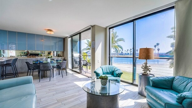 Un espace de vie moderne avec une table basse en verre, des canapés de couleur turquoise et une vue sur les palmiers, visible à travers de grandes fenêtres.