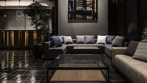 A modern interior with a sectional sofa, a coffee table, and a large window with a view of the cityscape. - Bespoke Hotel Shinsaibashi (Osaka)