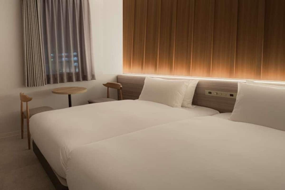 A hotel room with a large bed, a small round table, and a window with curtains.