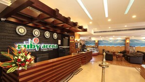A hotel reception area with a wooden reception desk, a clock, and a sign for "The Ruby Arena." - Hotel Ruby Arena (Thiruvananthapuram)