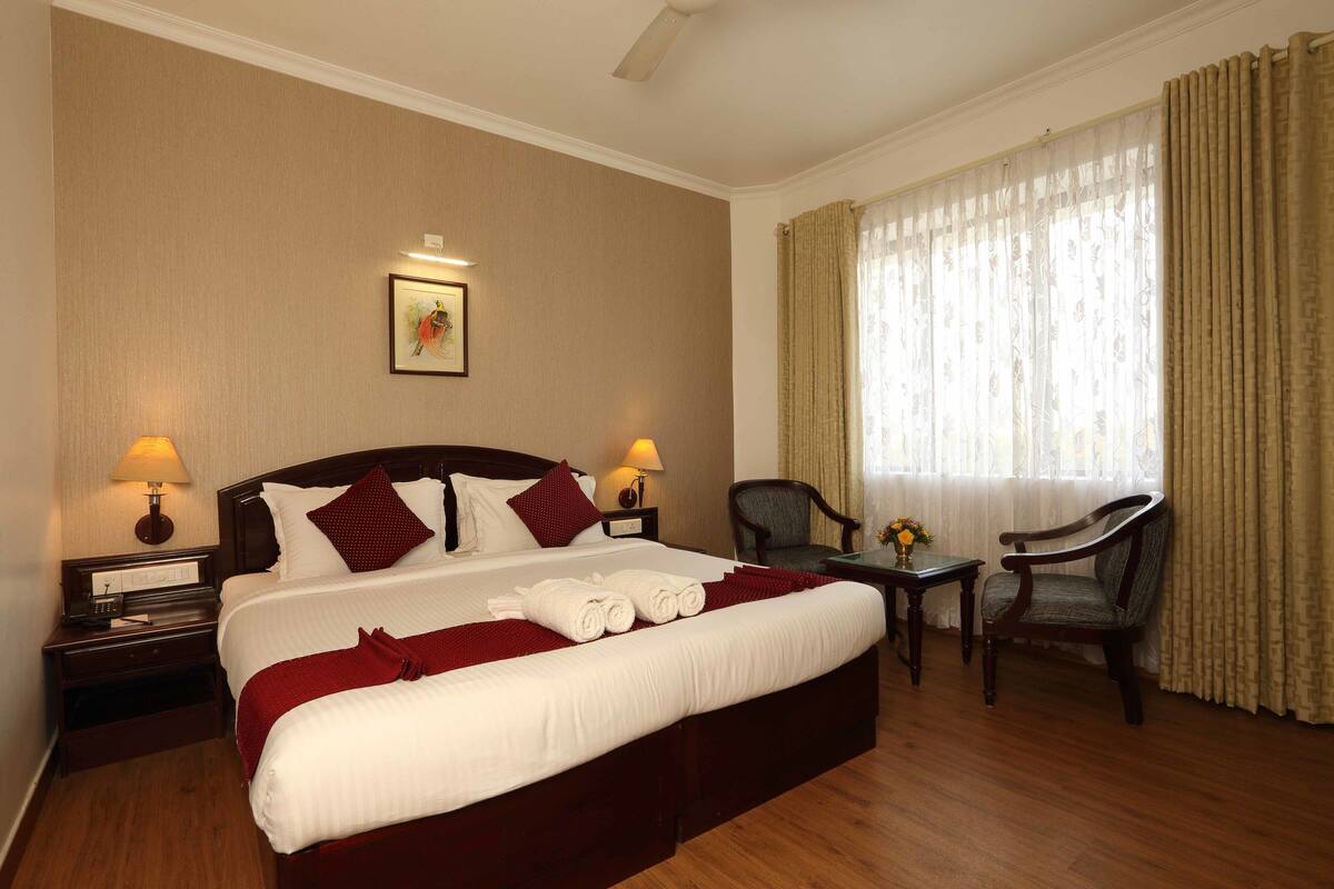 Une chambre d’hôtel avec un grand lit, deux tables de chevet avec des lampes, une chaise et une fenêtre avec des rideaux.