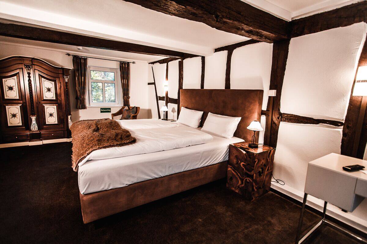A bedroom with a large bed, wooden headboard, and a nightstand with a lamp.
