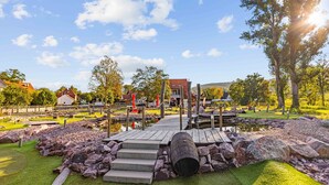 A wooden bridge leading to a dock over a pond, surrounded by rocks and grass. - Landhotel Kahltalmühle (Alzenau)
