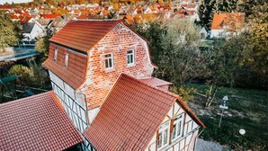 A traditional building with a red-tiled roof, surrounded by smaller houses and a hilly landscape. - Landhotel Kahltalmühle (Alzenau)