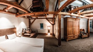 A bedroom with a large bed, wooden beams, a radiator, a cabinet, and a chair. - Landhotel Kahltalmühle (Alzenau)