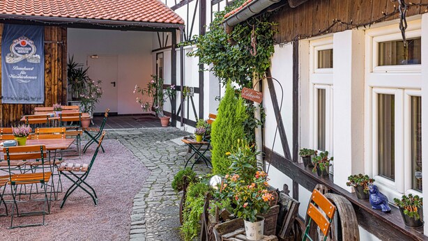 A courtyard with outdoor seating, potted plants, and a building with a sign. - Landhotel Kahltalmühle (Alzenau)