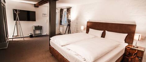 A hotel room with a large bed, a flat-screen TV mounted on the wall, a tripod, and a small table with a lamp.