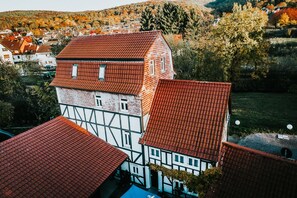 A traditional half-timbered building with a red-tiled roof, surrounded by other similar buildings and a hilly landscape in the background. - Landhotel Kahltalmühle (Alzenau)
