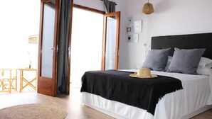 Une chambre à coucher avec un lit, une table de chevet, un luminaire suspendu et une vue sur l’extérieur, visible à travers une porte ouverte.