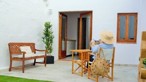 Une terrasse avec un banc en bois, une table et une personne qui lit un livre.