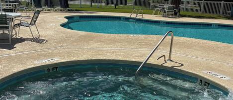 A swimming pool with a hot tub, surrounded by lounge chairs and a white fence.