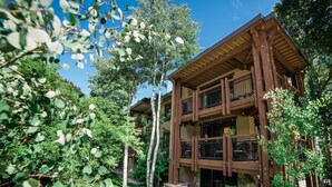 A multi-story wooden building with balconies, surrounded by lush greenery and trees. - Lift One - Stylish three bedroom with walk-out patio (Aspen)
