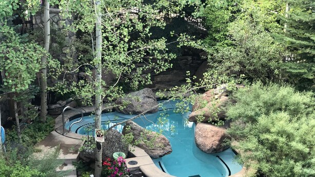 A hot tub surrounded by rocks and greenery, with a chair and table nearby. - Lift One - Stylish three bedroom with walk-out patio (Aspen)
