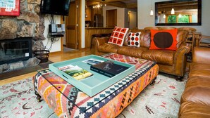 A cozy living room with a stone fireplace, leather sofa, and a colorful rug. - Lift One - Stylish three bedroom with walk-out patio (Aspen)