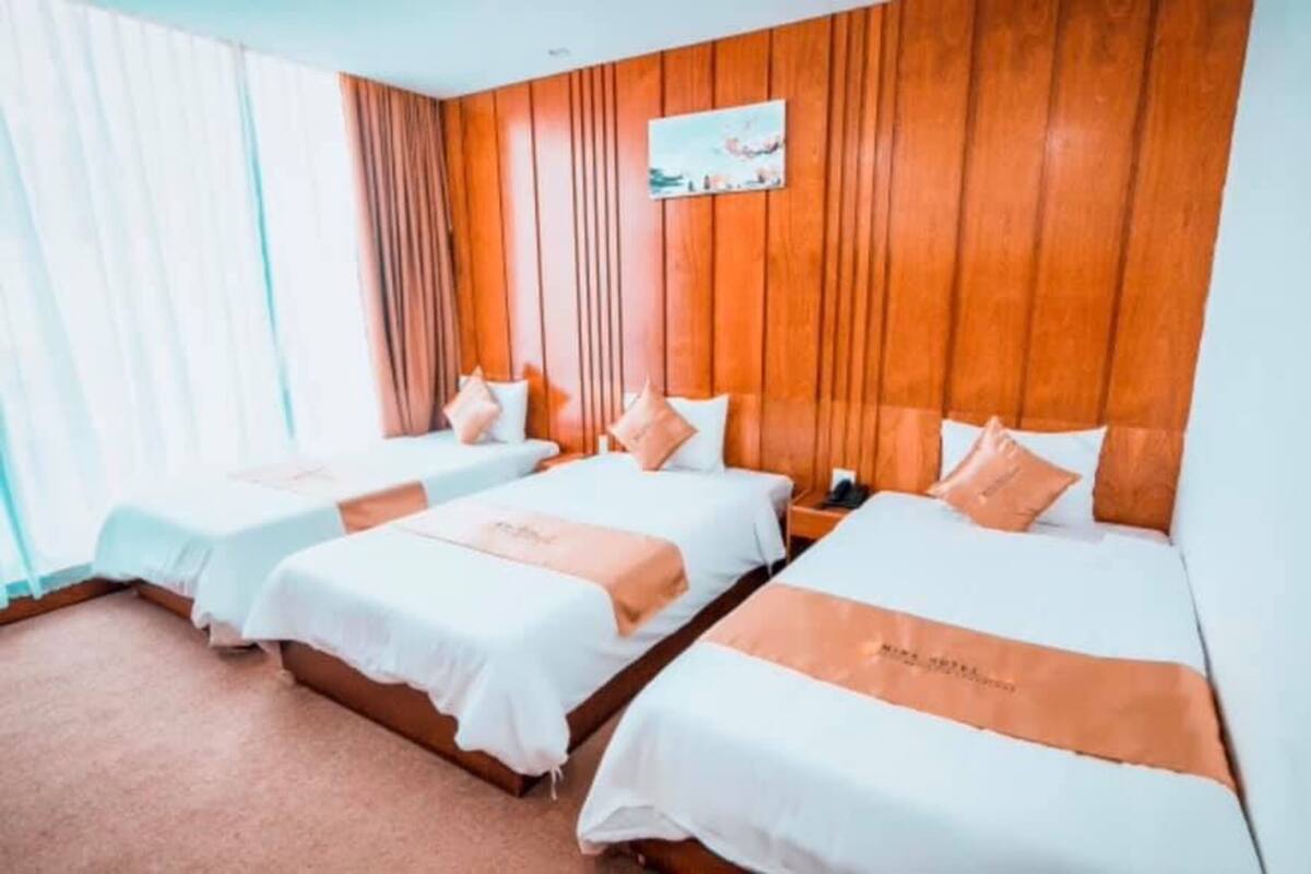 Une chambre d’hôtel avec trois lits, des murs recouverts de lambris en bois et un tableau au-dessus des lits.