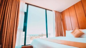 A hotel room with a large window, wooden panel walls, a bed with white linens, and a view of the outdoors. - Mira Hotel (Quy Nhon Nam)
