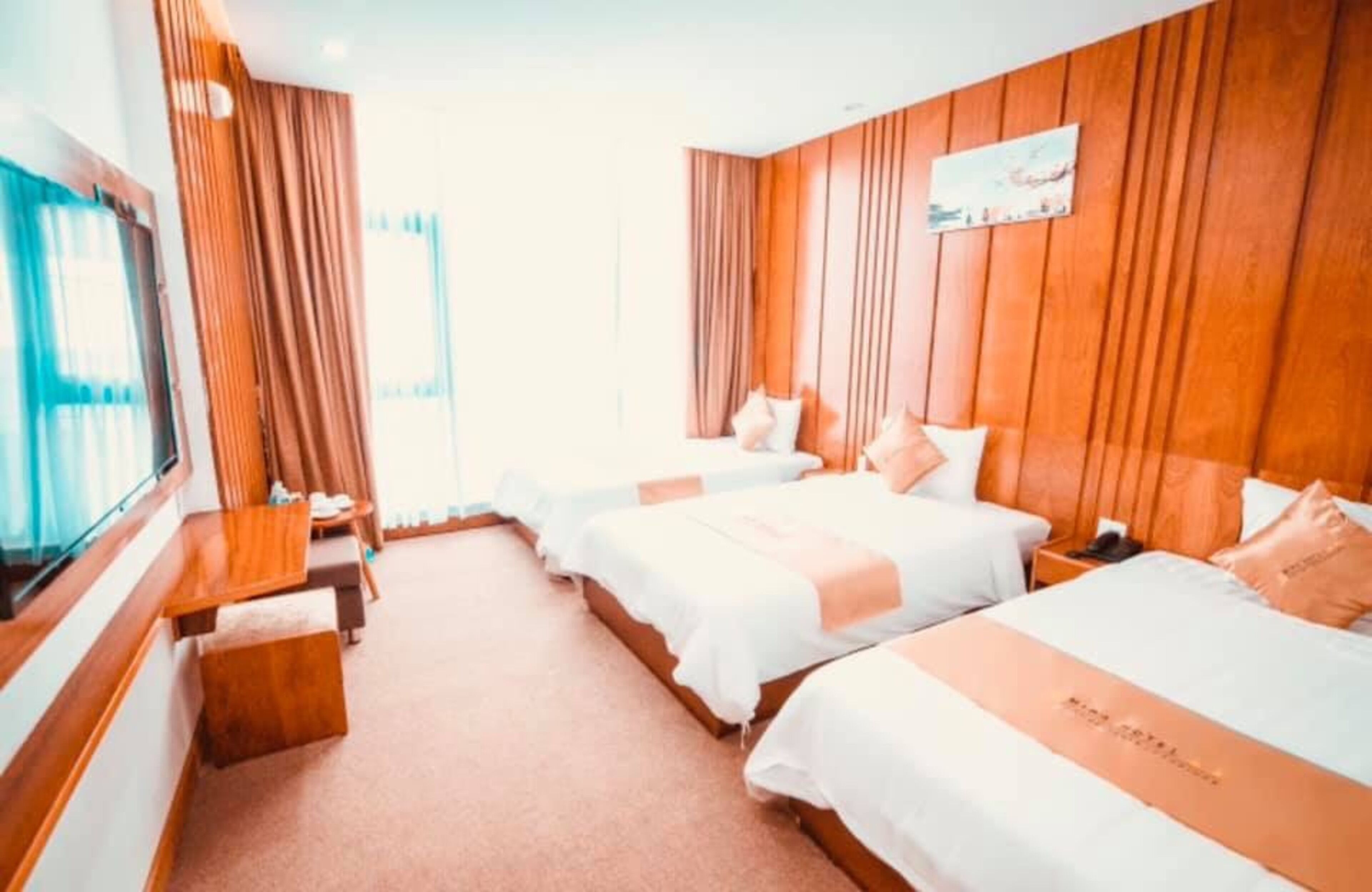A hotel room with two beds, a wooden headboard, a TV, and a window with curtains.