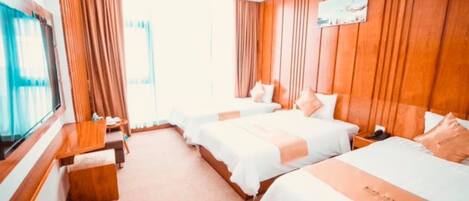 A hotel room with two beds, a wooden headboard, a TV, and a window with curtains.