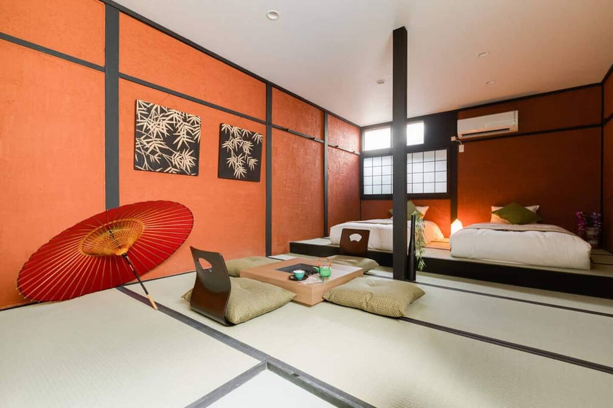 A traditional Japanese room with tatami flooring, a futon bed, a red folding fan, and wall art.