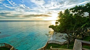 A coastal view with a wooden staircase leading to a beach area, surrounded by lush greenery and clear blue waters. - Parklane Bohol Resort and Spa (Anda)