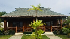 A rustic wooden house with a thatched roof, a small porch, and a well-maintained lawn. - Parklane Bohol Resort and Spa (Anda)