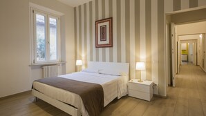 Ett sovrum med en säng, sängbord, ett fönster och en dörr som leder ut till en hall.