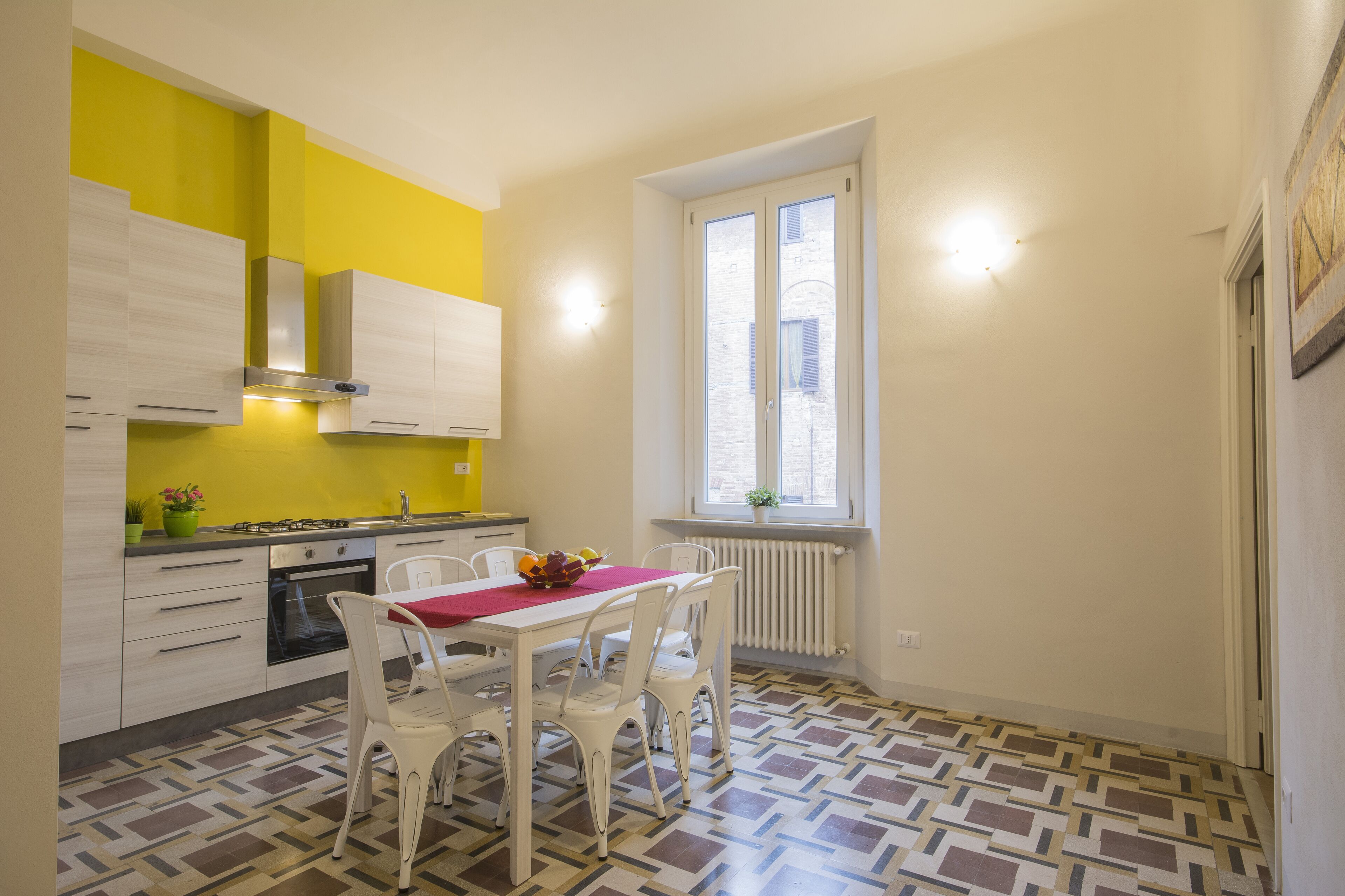 A compact kitchen with white cabinets, a yellow wall, and a dining area with a red tablecloth.
