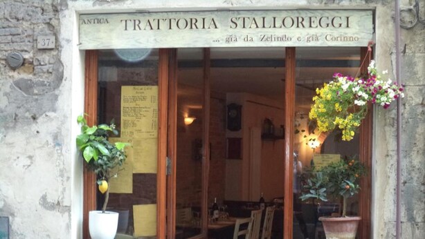Ingången till en restaurang som heter ”Antica Trattoria Stalloreggi”, med trädörrar, en menytavla och krukväxter utanför.