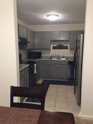 Compact kitchen with a refrigerator, microwave, and sink, adjacent to a dining area with a table and chairs.