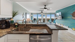 A kitchen with a stainless steel sink, a dishwasher, and a coffee maker. There is a ceiling fan and a view of the ocean through large windows. - Breezeway-Gulf Front Home Sleeps 9 (Navarre)