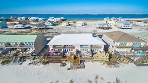 A beachfront property with multiple buildings, a large central structure with a flat roof, and a sandy beach in the foreground. - Breezeway-Gulf Front Home Sleeps 9 (Navarre)